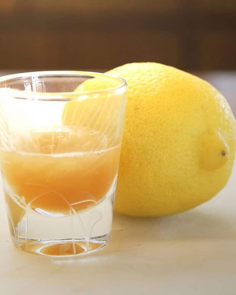 Image of shot glass with lemon juice and psilocybin mushrooms next to a full lemon.