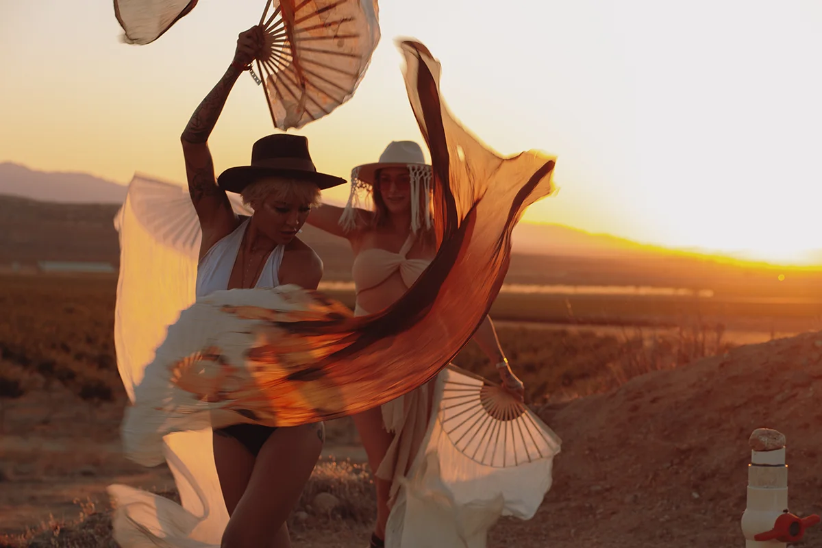 two people dancing with fans in front of desert sunset at Doubleblind Mycologia festival