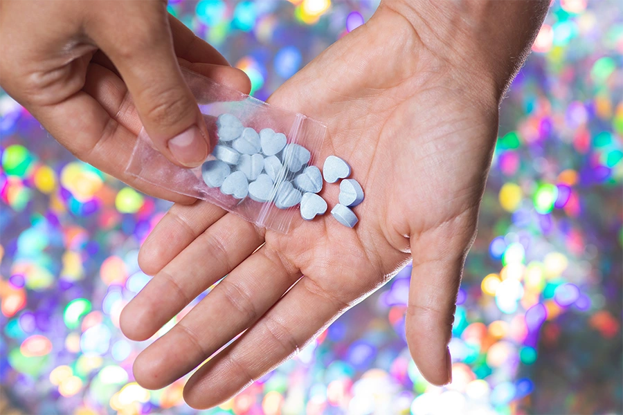 hand pouring out blue ecstacy pills onto palm with sparkly background