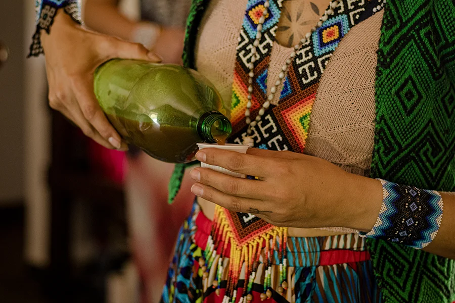shaman pouring ayahuasca brew out of green plastic bottle into small cup