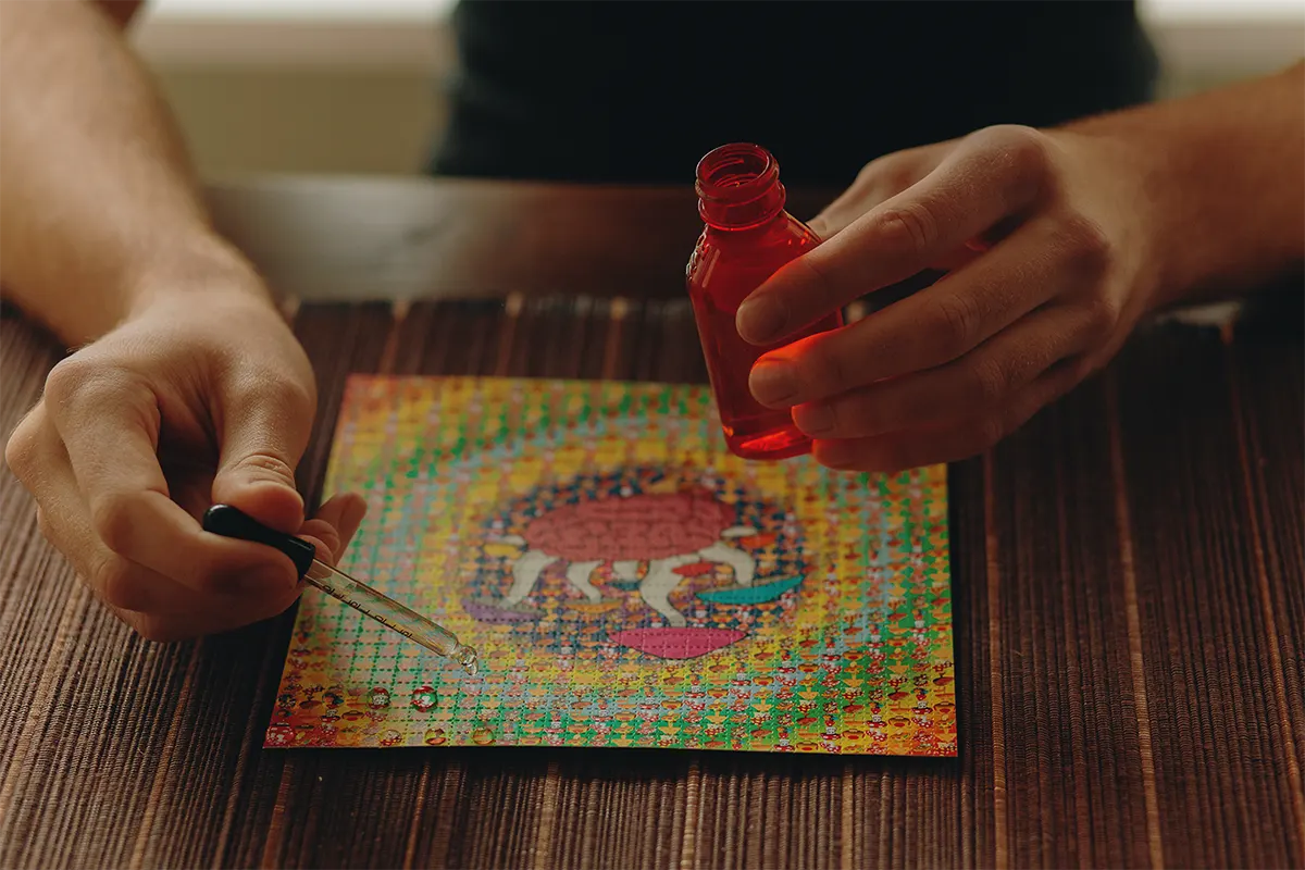 person holding vial of LSD placing drops on to LSD blotter paper